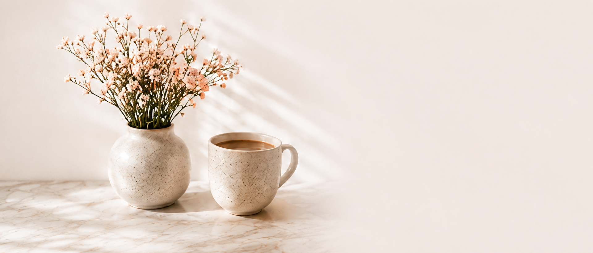 A ceramic vase of pink baby's breath flowers and a mug of coffee on a marble table in soft light